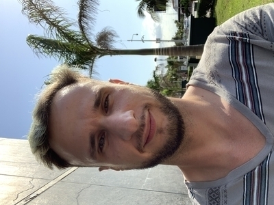 The author, hair dyed blue, standing in front of a palm tree, squinting due to the tropical sun.